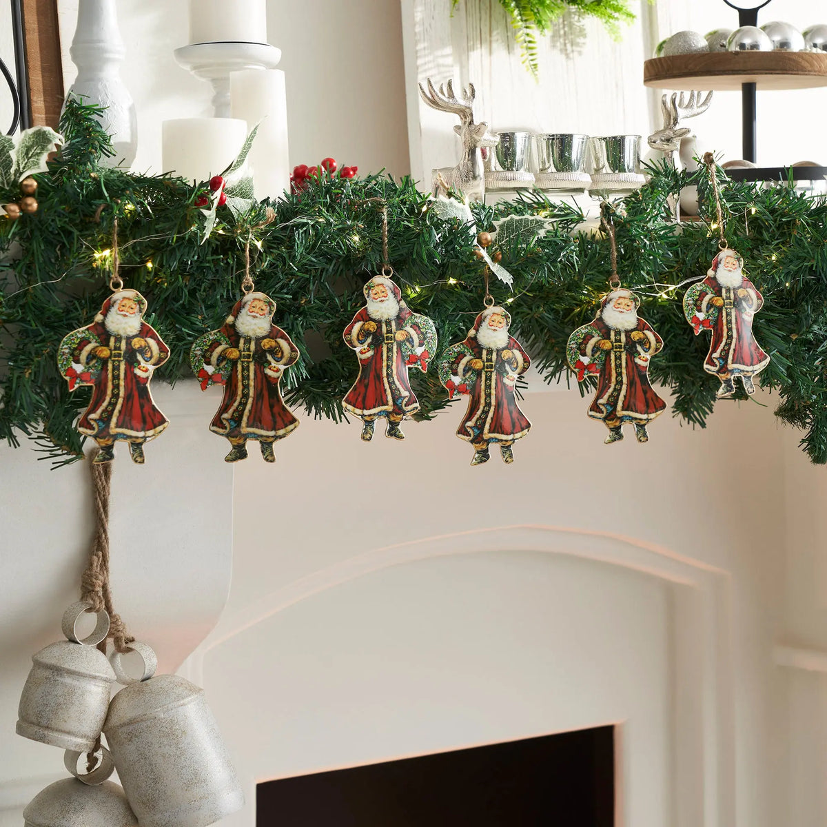 Jolly Old St Nick Metal Ornament Set of 6 - 5.5 inch set on garland on a white fireplace with a large silver bell, and two silver reindeer