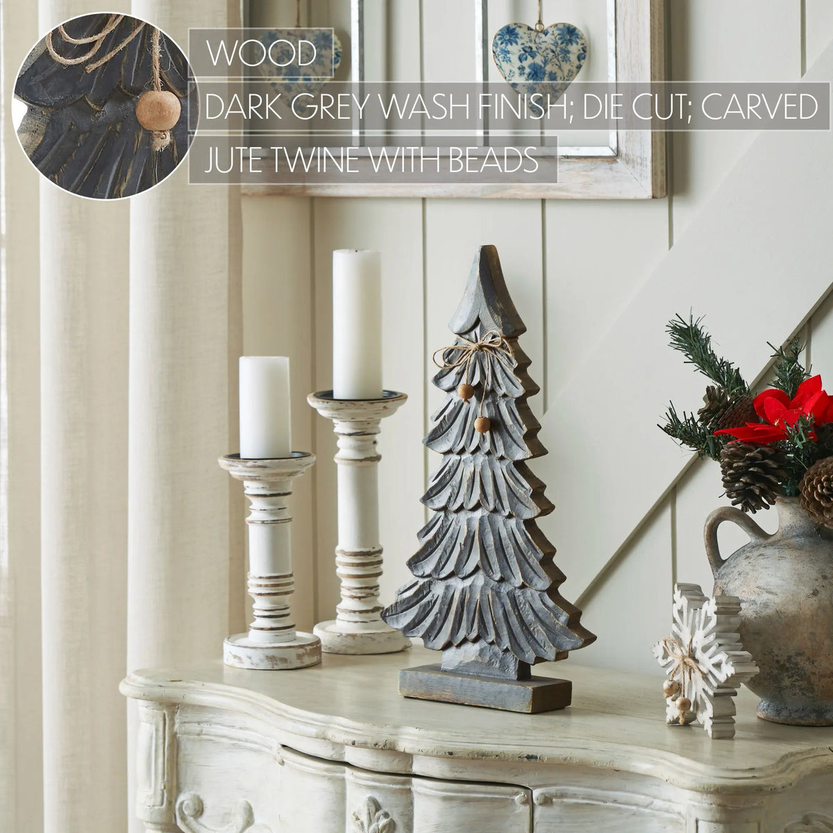 A dark grey-washed wooden Christmas tree centerpiece with carved details and a small jute twine bow, styled on a distressed cream console table alongside white pillar candles and holiday decor. Text overlay reads 'WOOD: DARK GREY WASH FINISH; DIE CUT; CARVED JUTE TWINE WITH BEADS'.