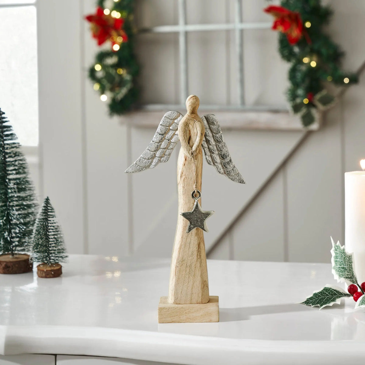 Wooden angel figurine with star on a white surface, Christmas decorations in the background