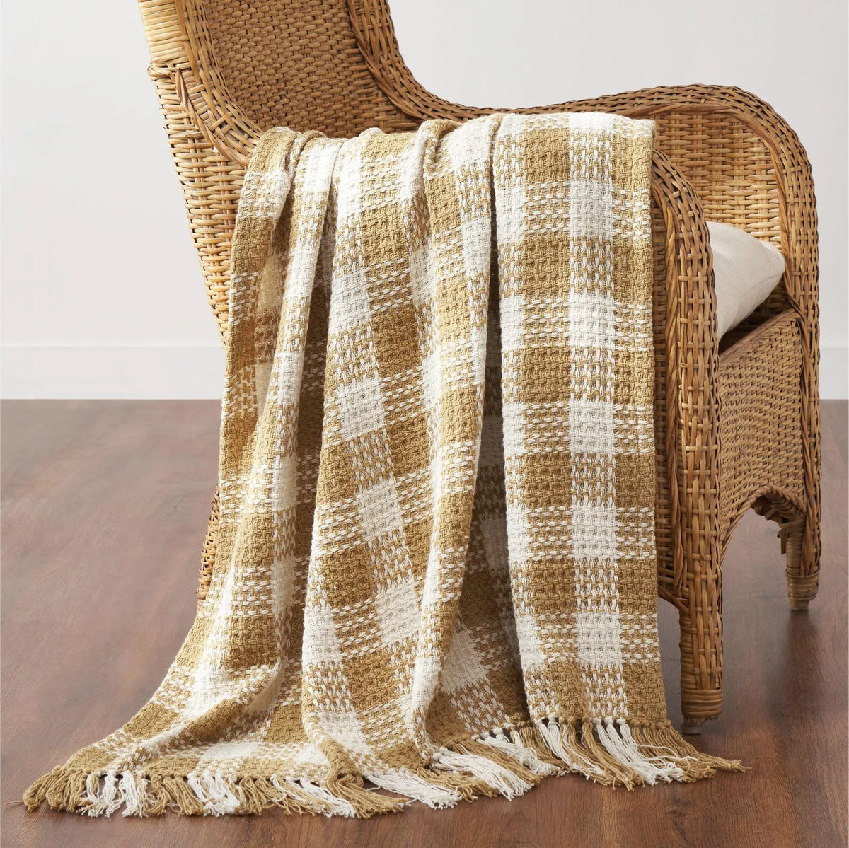 Plaid blanket draped over a wicker chair on a wooden floor.