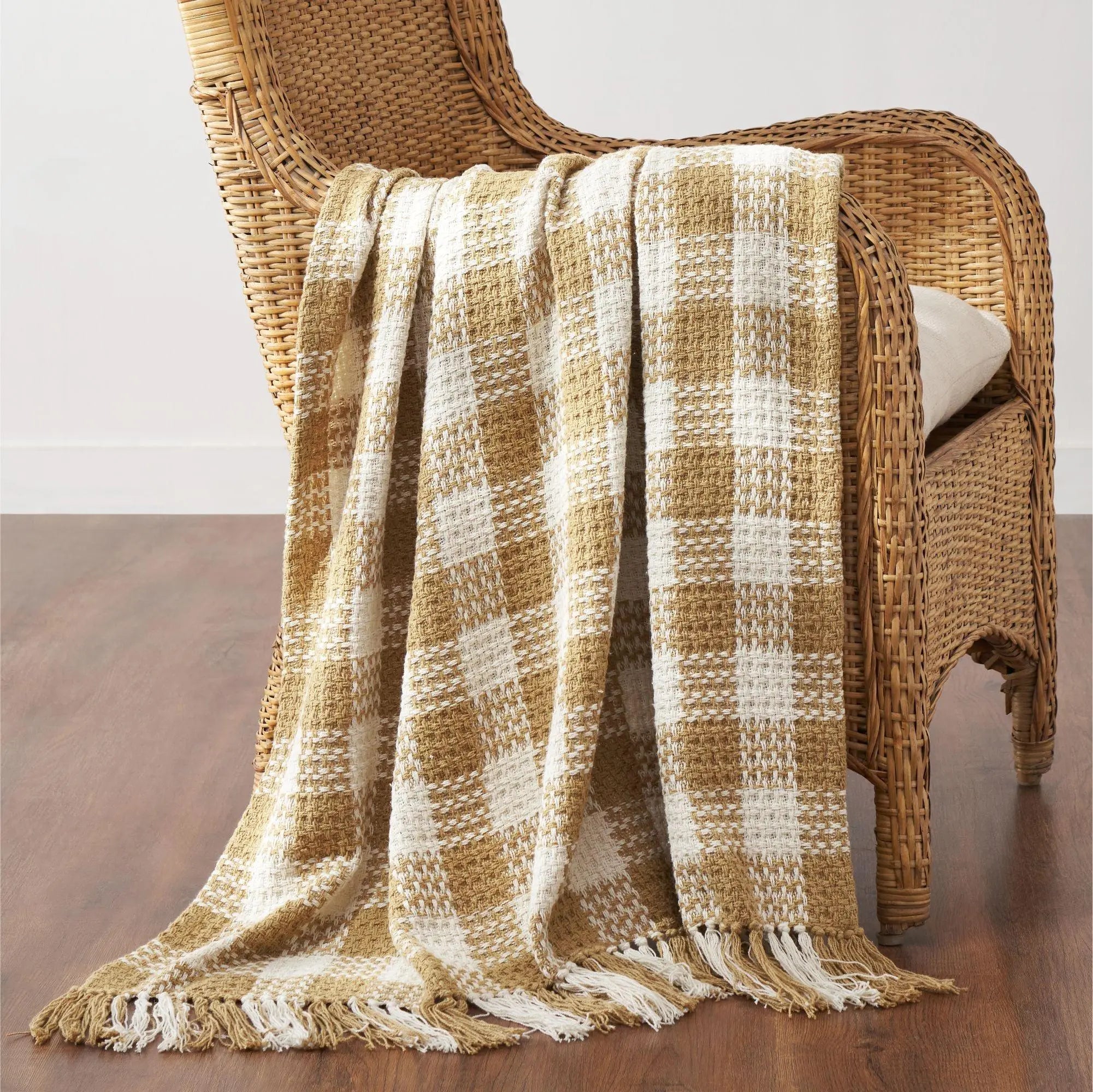 Plaid blanket draped over a wicker chair on a wooden floor.
