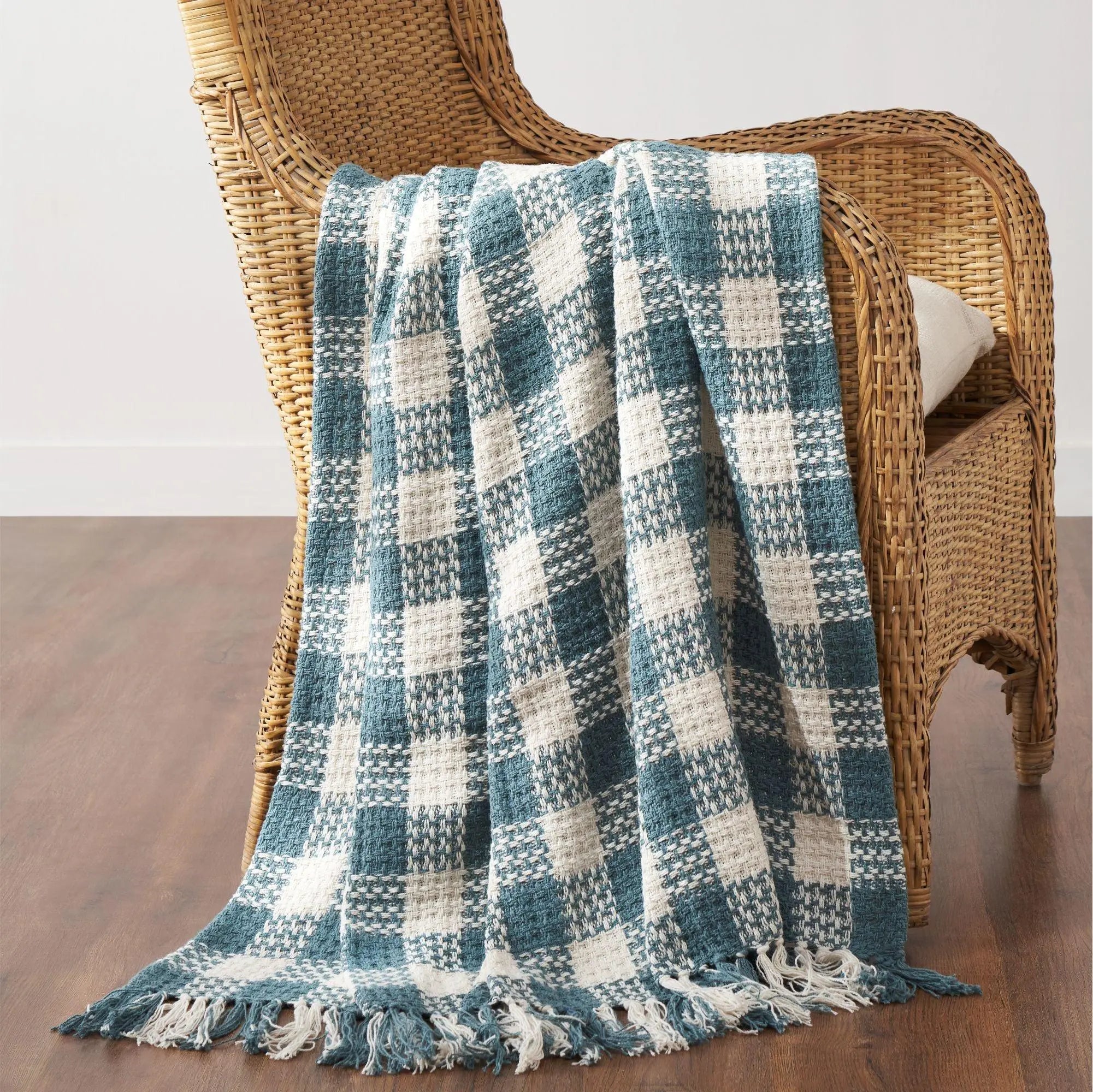 Blue and white checkered blanket draped over a wicker chair on a wooden floor.