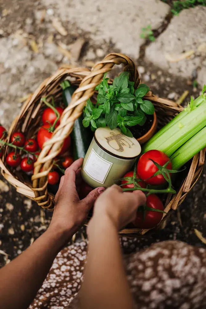 Cozy farmhouse candle in wicker basket with fresh tomatoes, basil, and celery for rustic home decor
