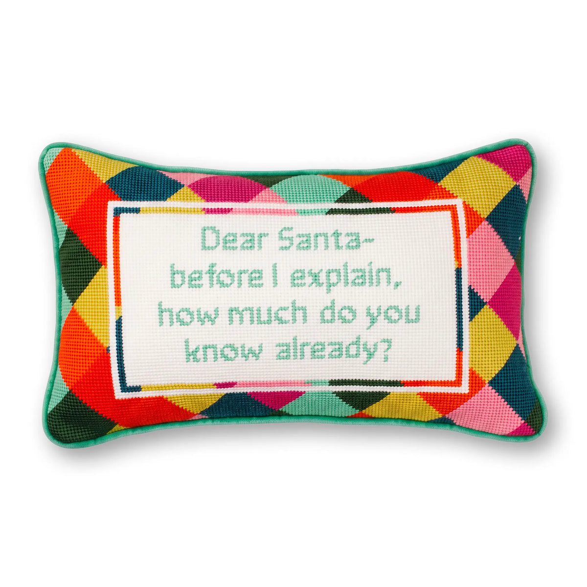 A rectangular decorative pillow with a colorful geometric diamond pattern in red, orange, yellow, green, blue, and pink. The center features a white square panel with a teal embroidered message that reads, 'Dear Santa - before I explain, how much do you know already?'.