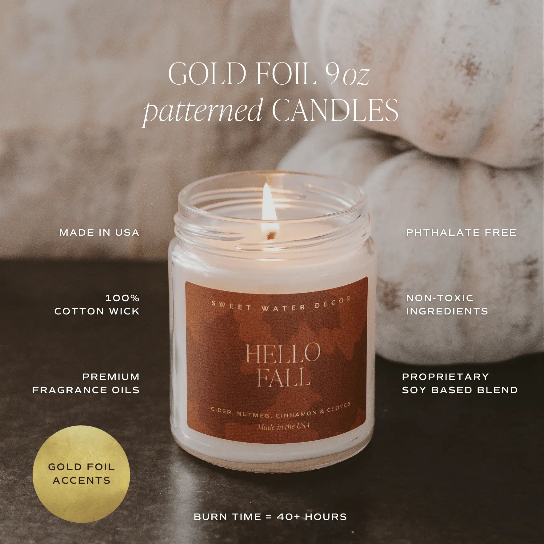 Candle with 'Hello Fall' label on a dark surface, surrounded by pumpkins.