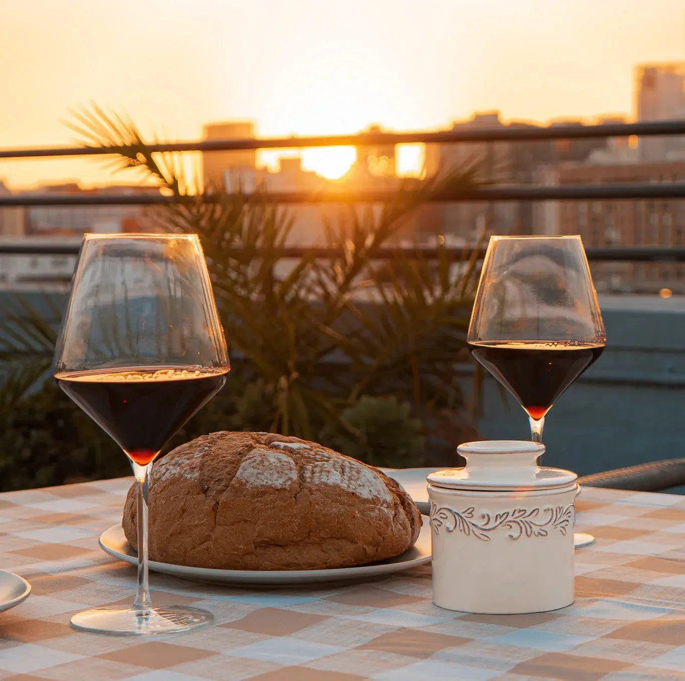 Cozy rooftop dinner with red wine, rustic bread, and ceramic jar at sunset, farmhouse style table setting