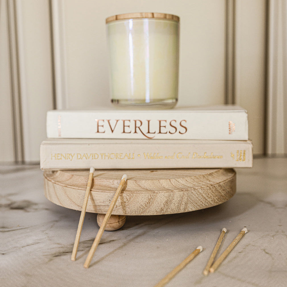 Stack of books titled 'Everless' and 'Henry David Thoreau' on a wooden stand with a candle in the background.