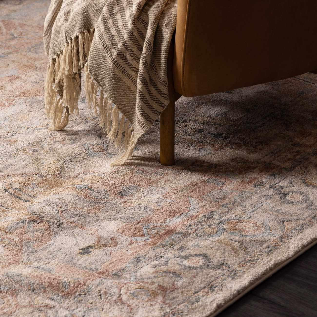 Cozy farmhouse rug with vintage pattern, draped throw blanket, and wooden chair leg on warm-toned floor