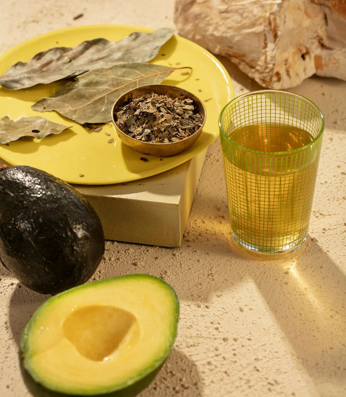 Avocado, glass of juice, and dried herbs on a textured surface