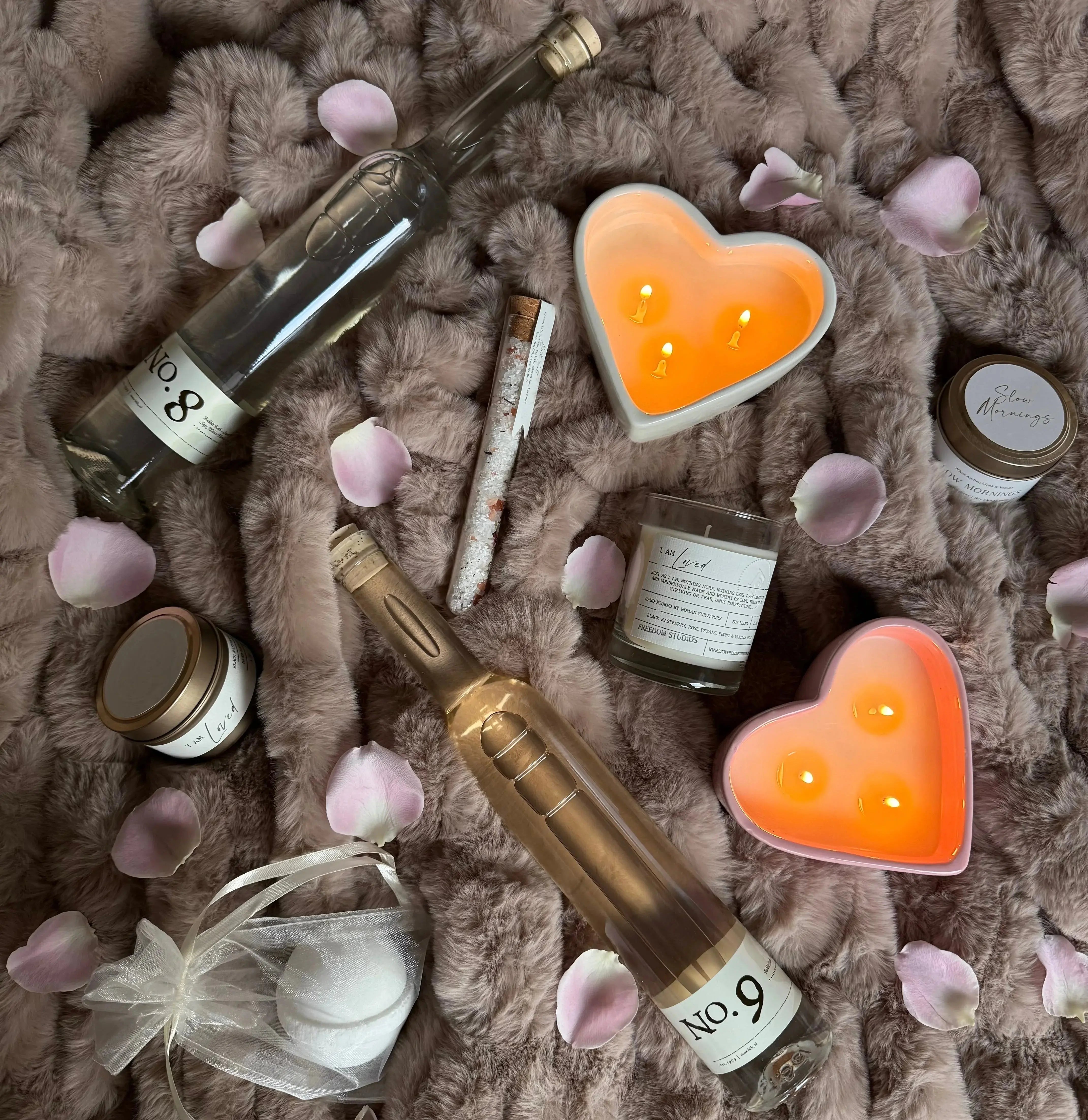 Cozy farmhouse bath & candle set with heart-shaped candles, rose petals, and luxury bath products on a plush blanket
