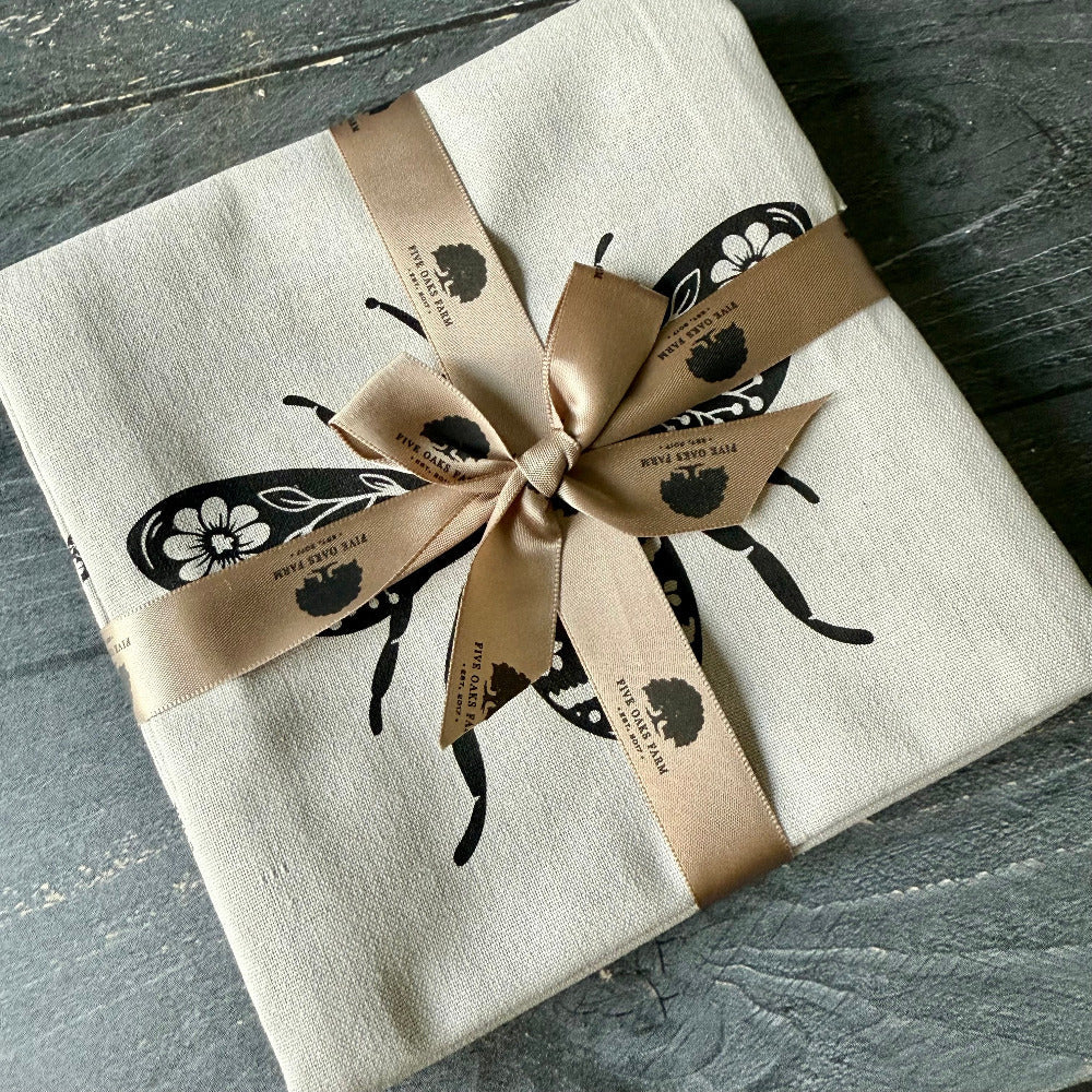 Gift wrapped in beige paper with black beetle design and gold ribbon on a wooden surface