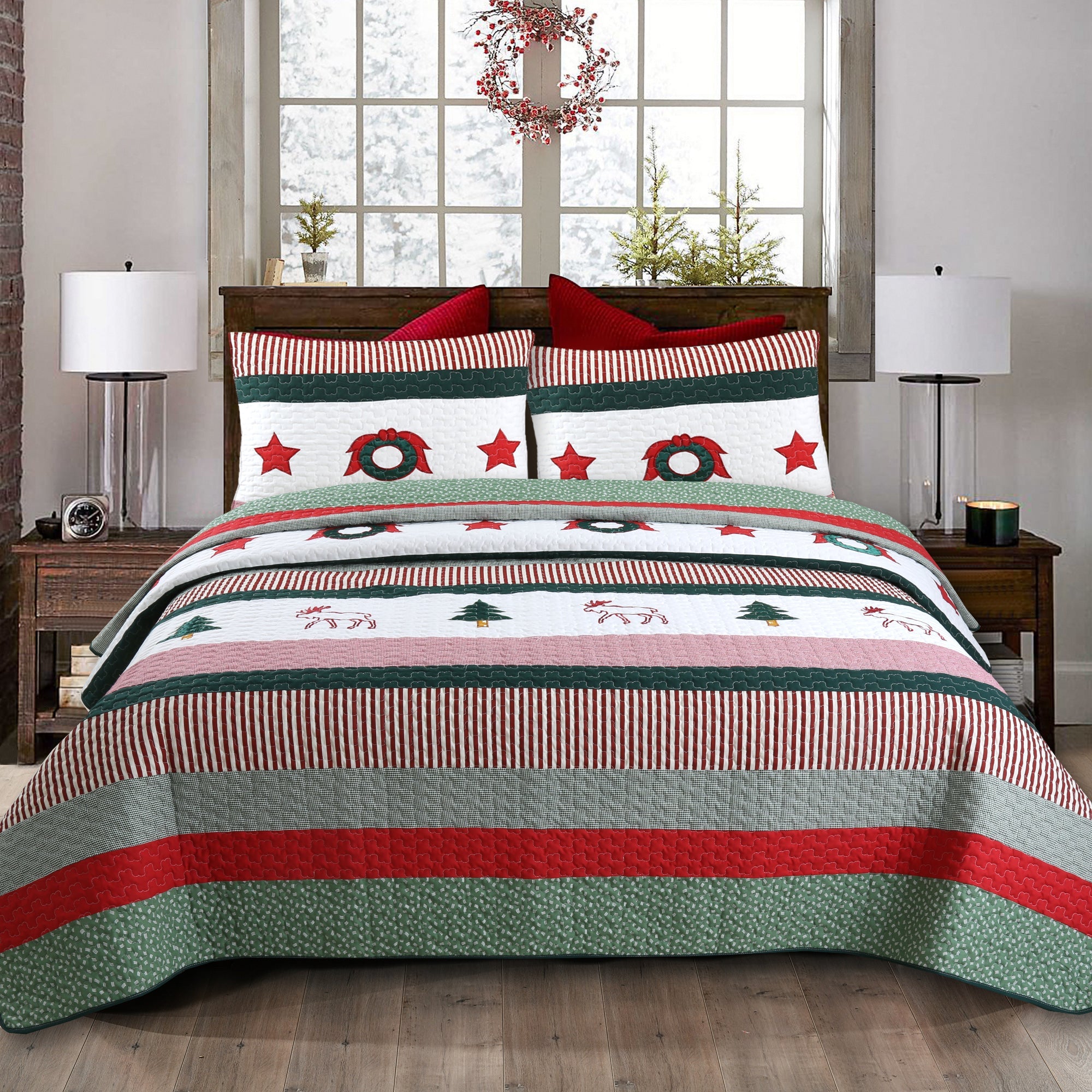 A festive Christmas-themed bedding set displayed on a bed in a styled bedroom. The set includes a quilt and two matching pillow shams with a pattern of red stripes, green wreaths, red stars, and small holiday tree and reindeer motifs on a white background.