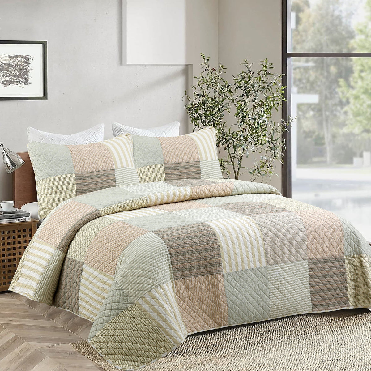 A patchwork quilted bedding set in soft beige, sage green, and brown tones, styled on a bed in a modern bedroom setting with a window, plant, and wooden headboard.