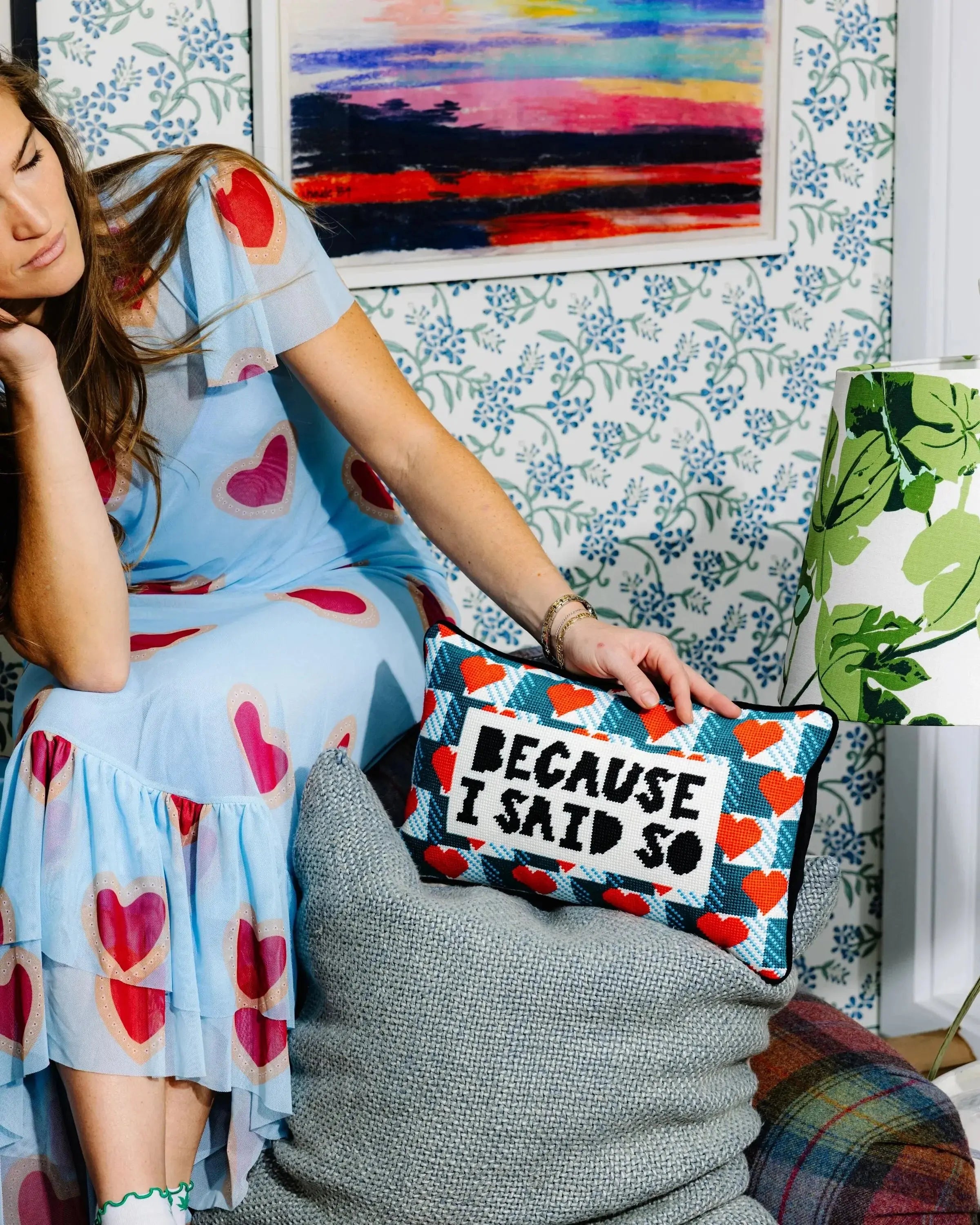 Woman holding a pillow with 'BECAUSE I SAID SO' text in a room with colorful decor.