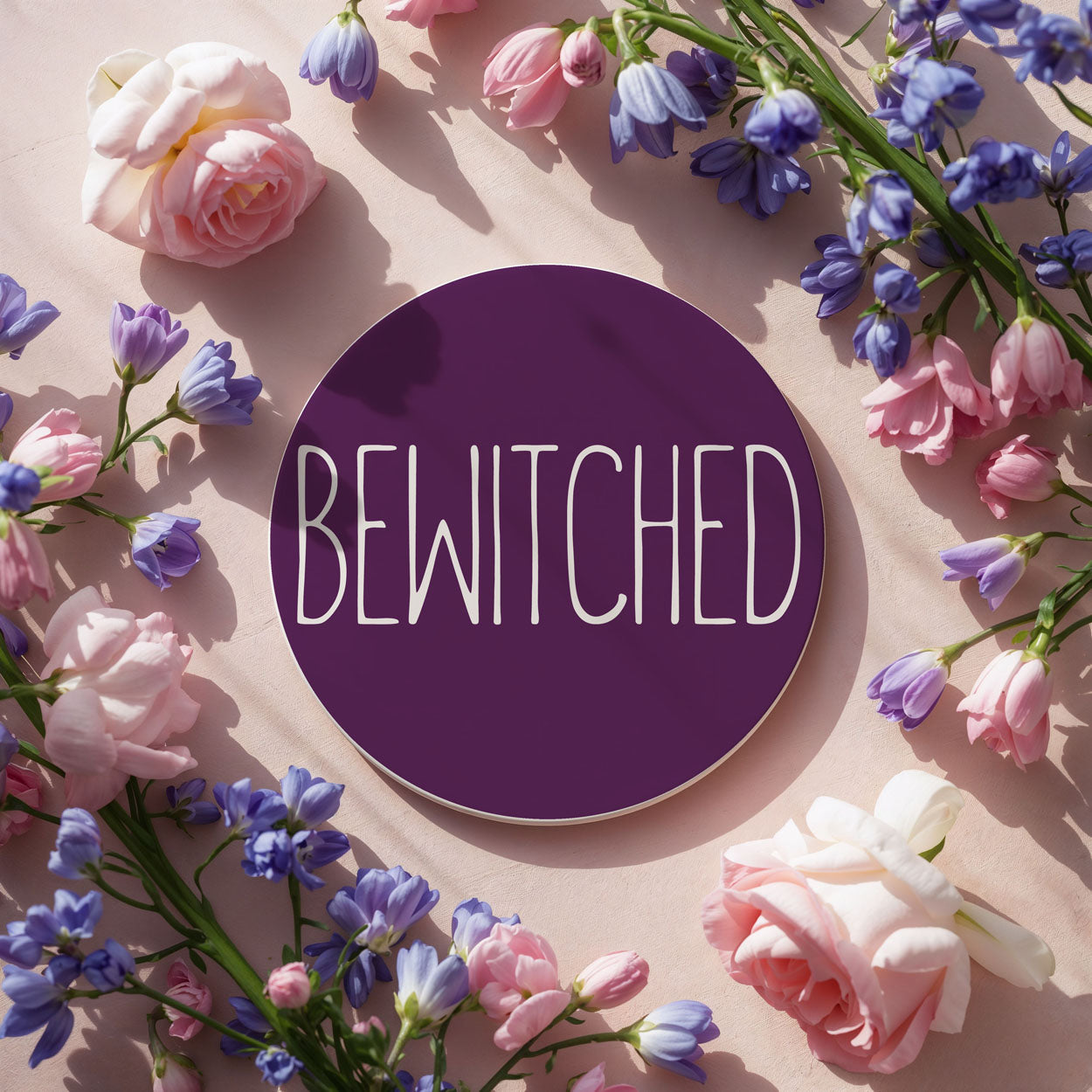 Floral arrangement with a purple 'BEWITCHED' label on a light pink background