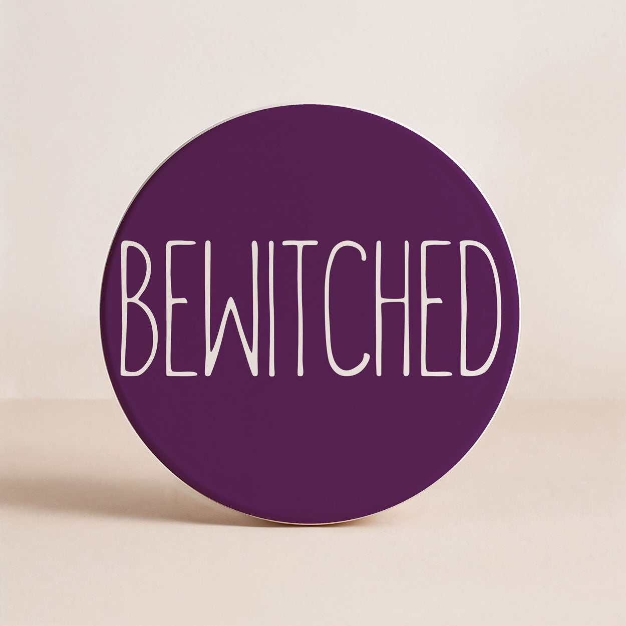 Round purple coaster with 'BEWITCHED' text on a beige background