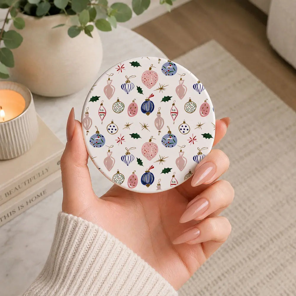 Hand holding a round decorative item with Christmas ornament pattern on a neutral background