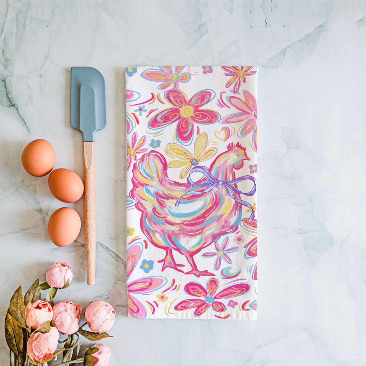 Colorful towel with chicken and floral design on a marble surface with eggs and a spatula.