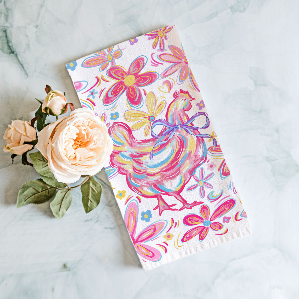 Colorful rooster and floral patterned towel on a marble surface with flowers.