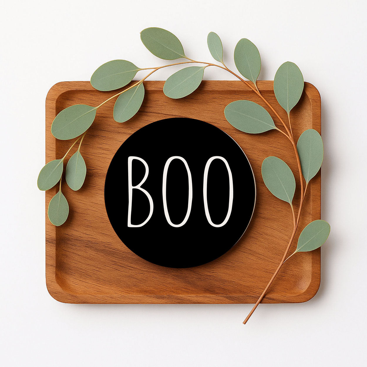 Wooden tray with a black circle displaying 'BOO' and green leaves on a white background