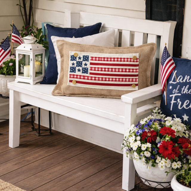 Decorative bench with American flag-themed pillows and flags on a wooden deck.