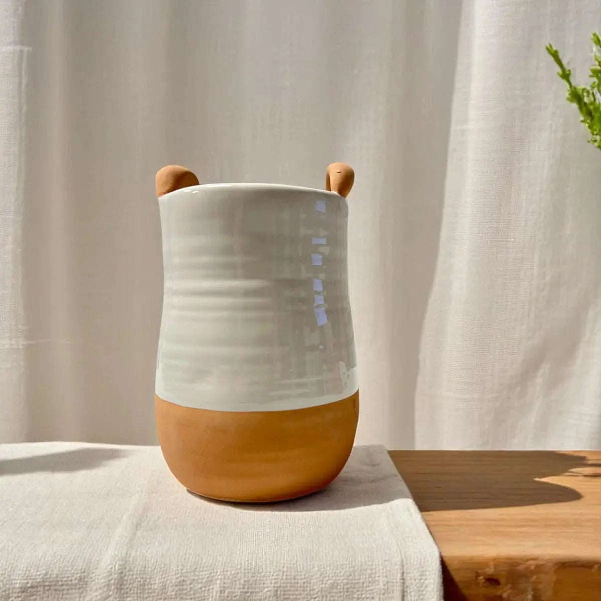 White and brown ceramic vase with bear ears on a wooden surface