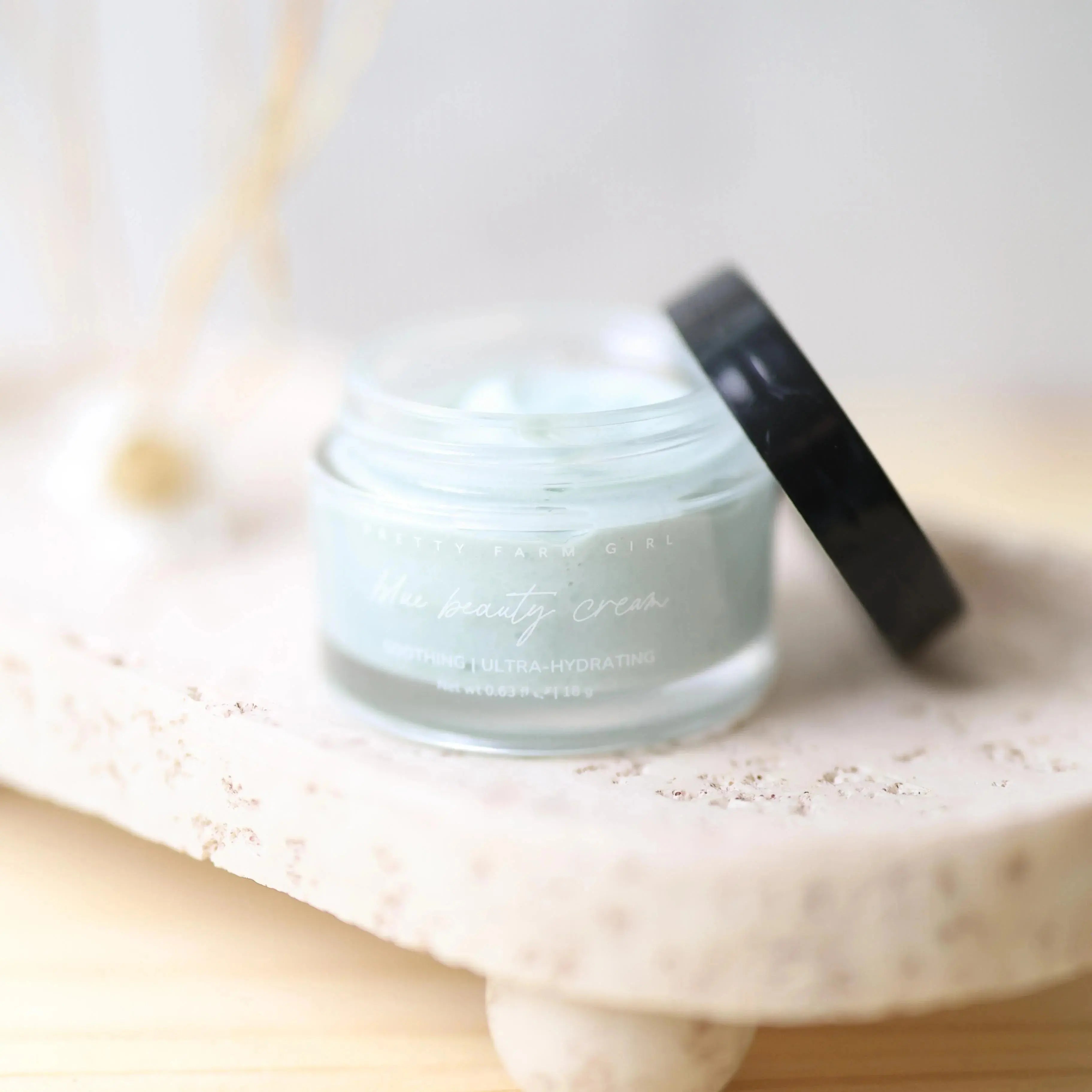 Pretty Farm Girl Mue beauty cream, soothing ultra-hydrating face moisturizer in glass jar with black lid on stone tray