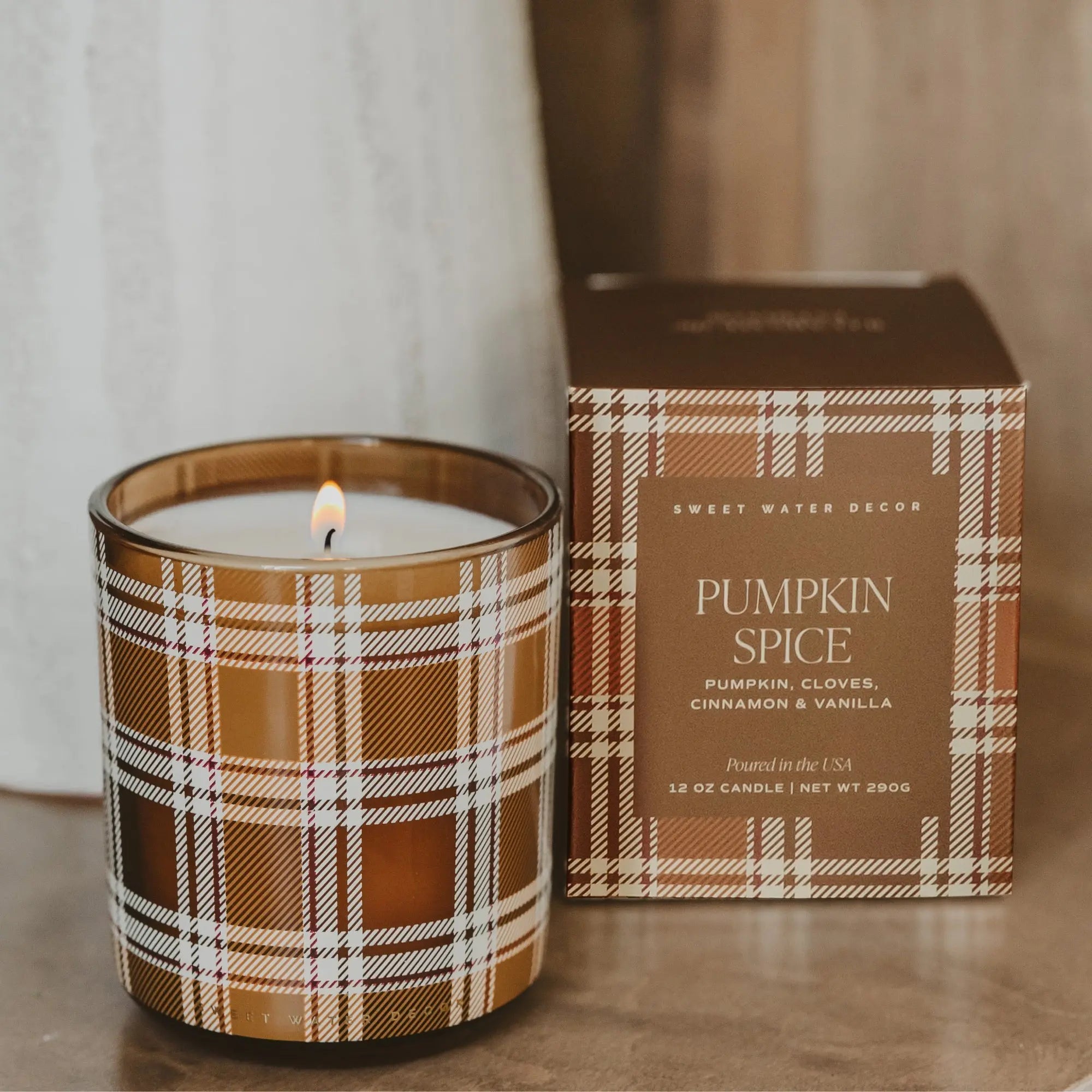 Candle with plaid design and packaging labeled 'Pumpkin Spice' on a wooden surface.