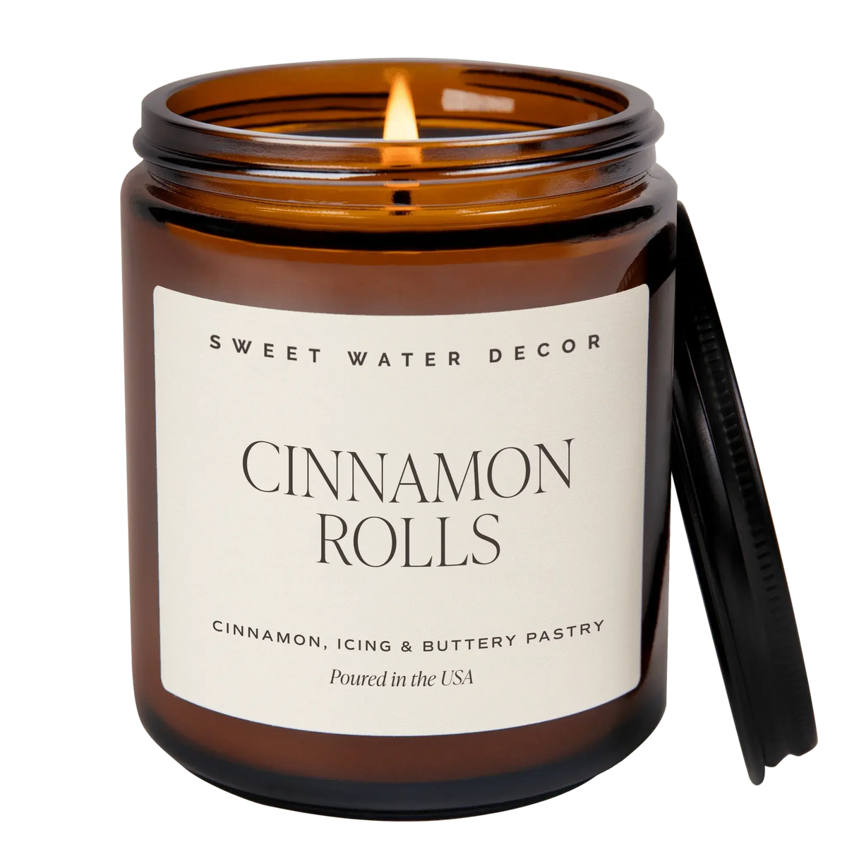Candle in an amber jar labeled 'Cinnamon Rolls' by Sweet Water Decor on a white background
