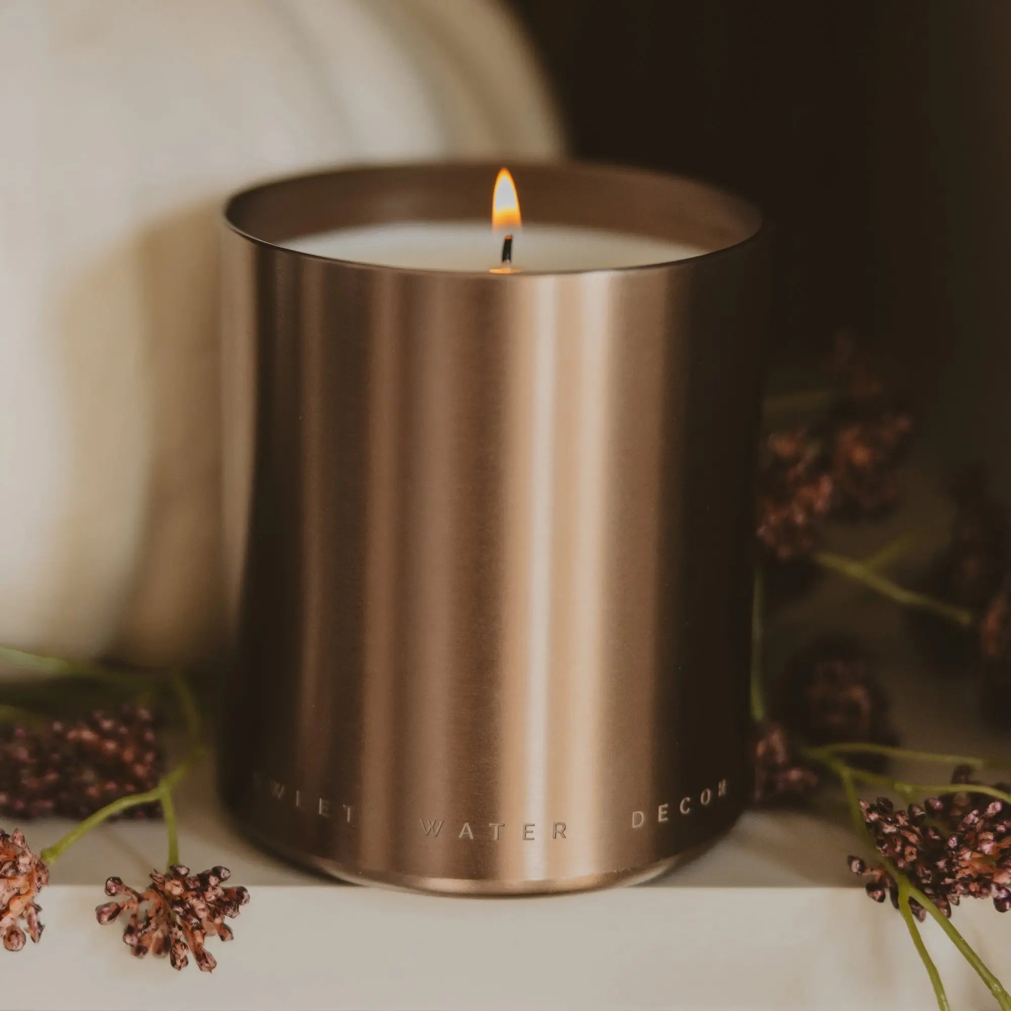 Candle in a bronze container with decorative elements on a neutral background