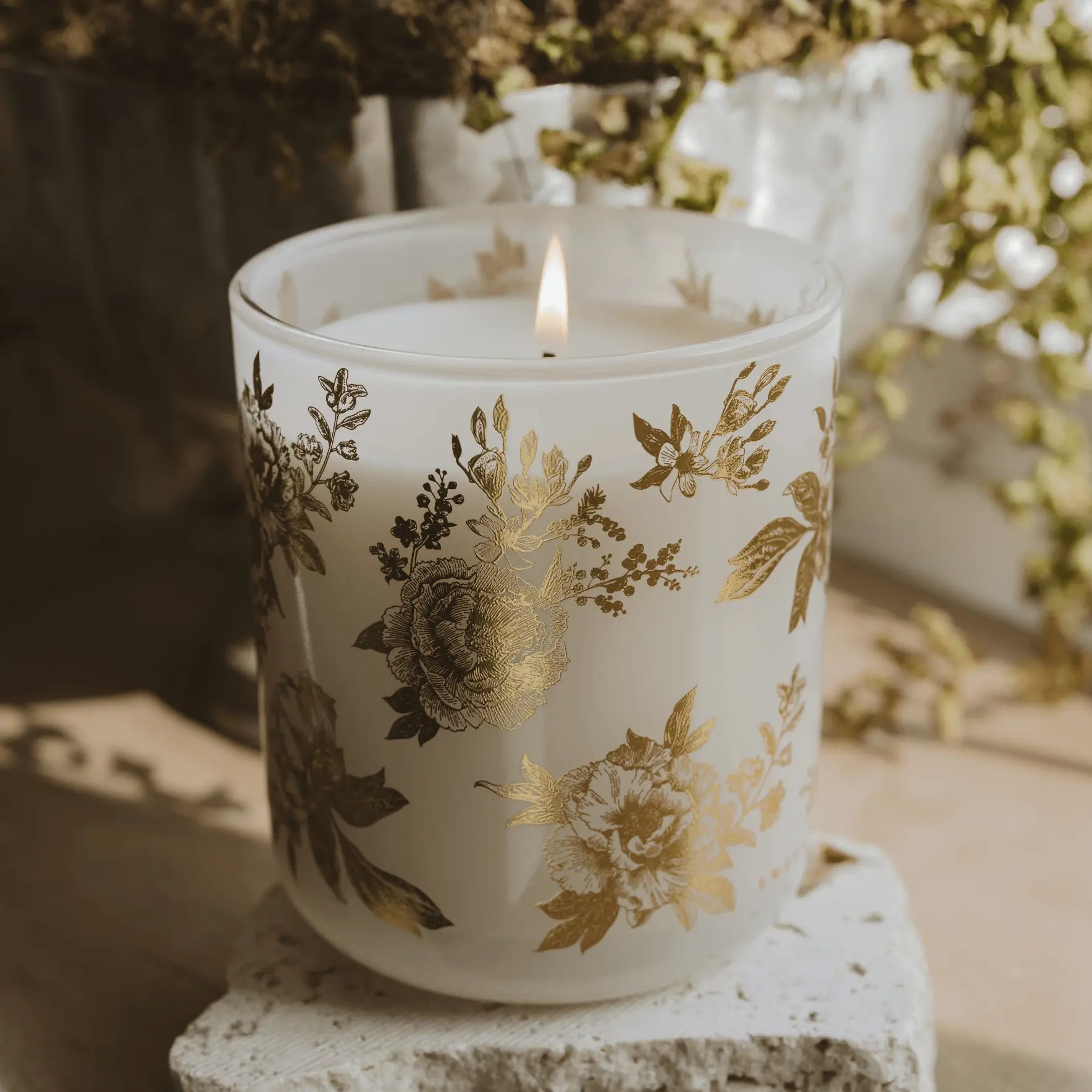Lit floral candle in frosted glass with gold botanical print, cozy farmhouse decor