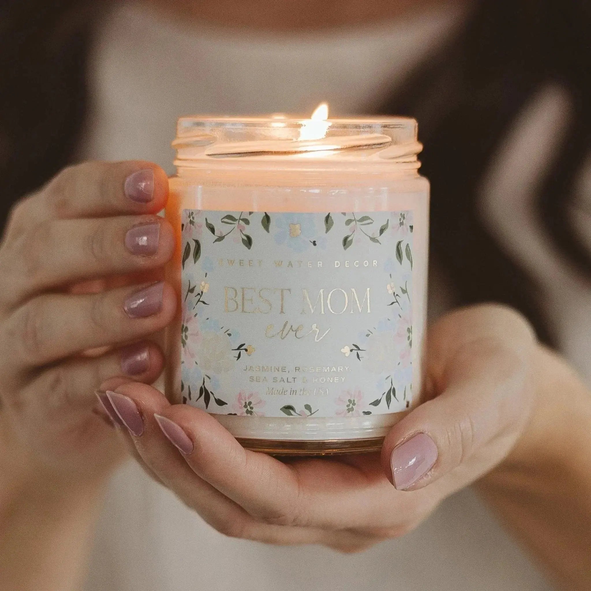 Best Mom Ever scented candle with floral label, held in hands, jasmine rosemary sea salt honey fragrance