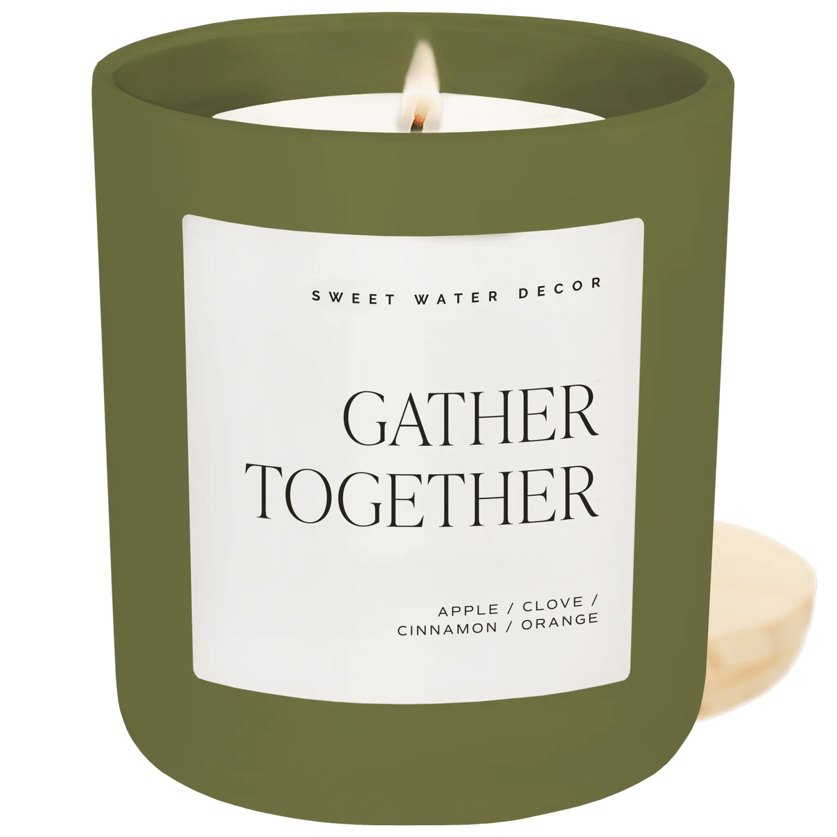 A lit candle in an olive green jar with a white label reading 'GATHER TOGETHER' and 'SWEET WATER DECOR,' shown on a solid green background with a small cream-colored candle piece at the lower right.