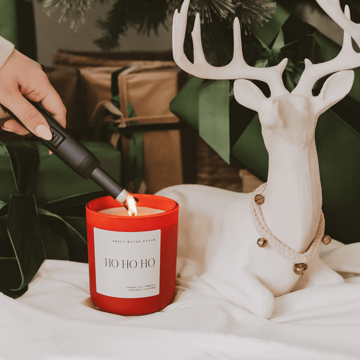 Person lighting a red candle labeled 'Ho Ho Ho' next to a decorative deer figurine.