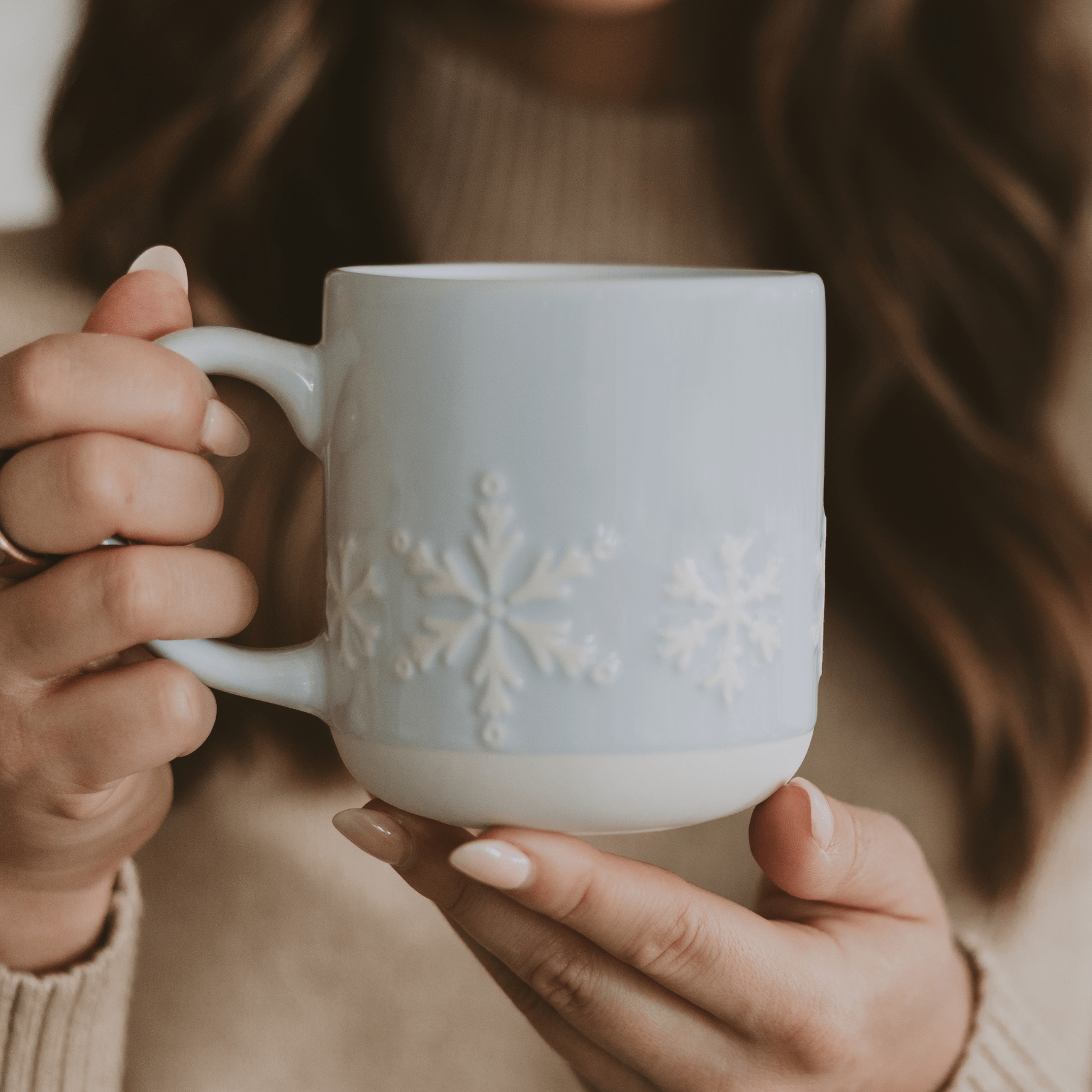 Person holding a white mug with snowflake design, blurred background