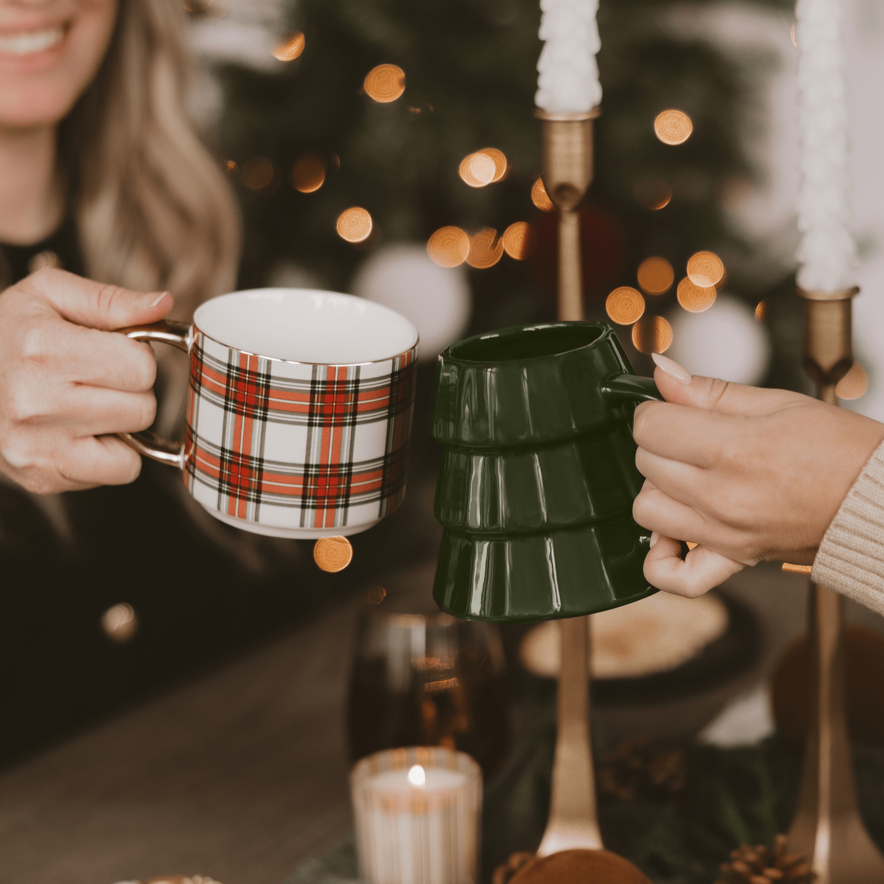 Two people holding mugs with a festive background featuring candles and lights.