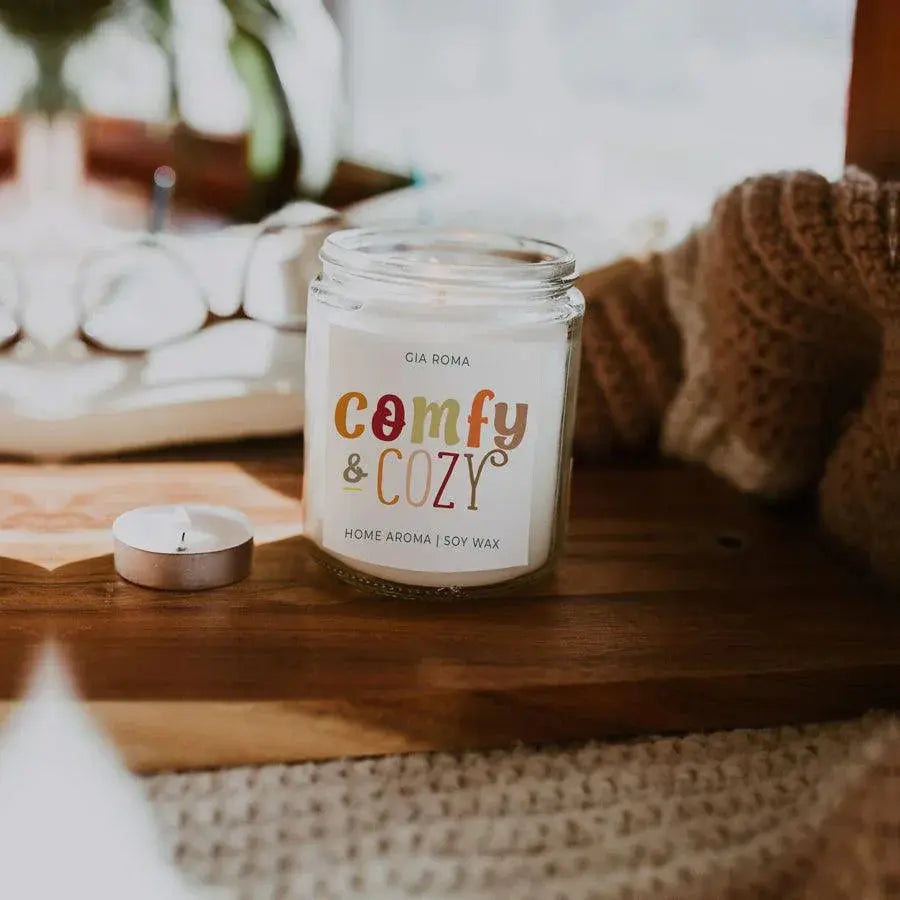 Candle jar labeled 'comfy & cozy' on a wooden surface with a blurred background
