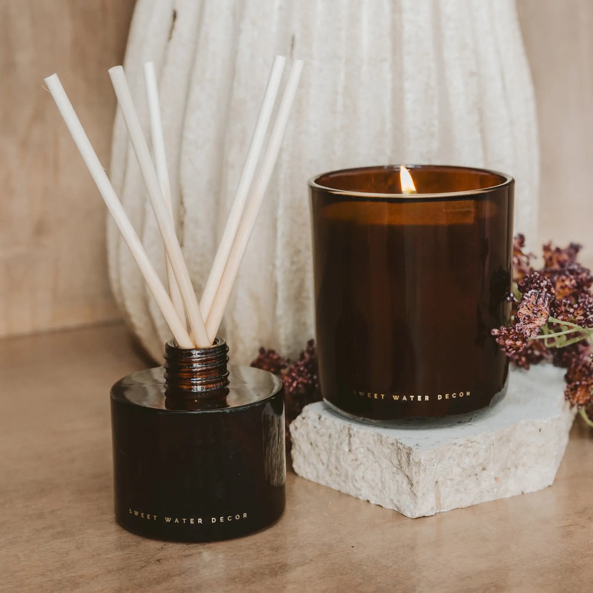 Decorative candle and diffuser set on a wooden surface with a neutral background