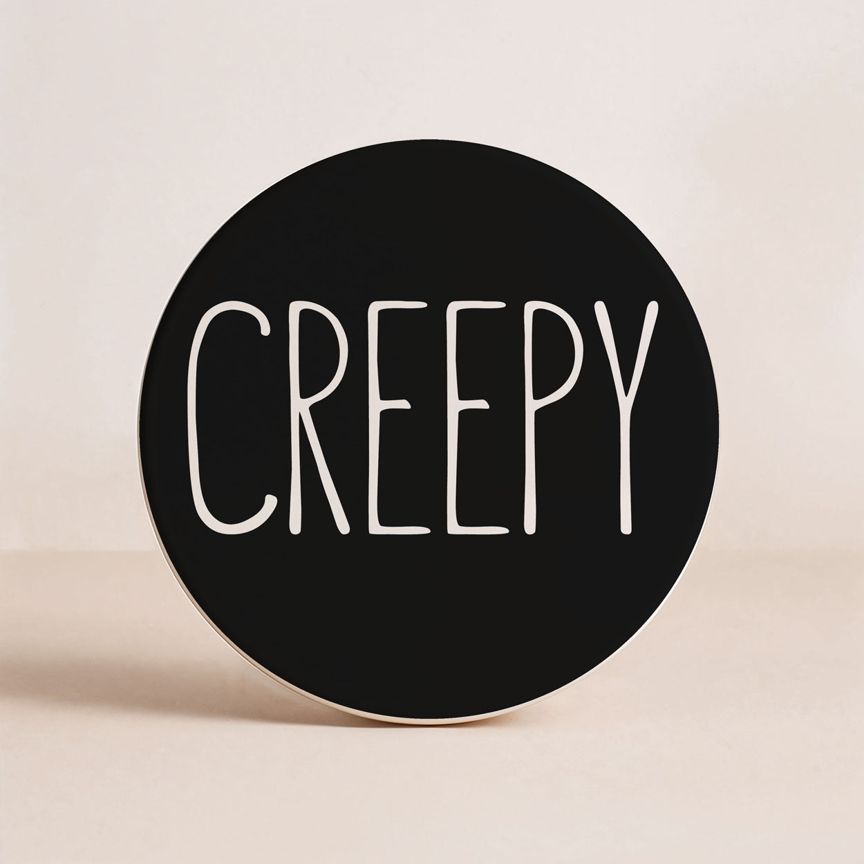 Round black sign with 'CREEPY' in white text on a beige background