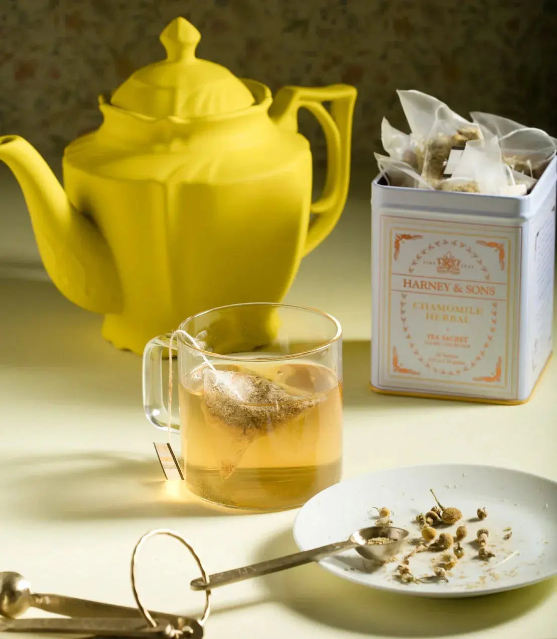 Yellow teapot with chamomile herbal tea in glass mug, tea tin, and dried flowers for cozy cottage decor
