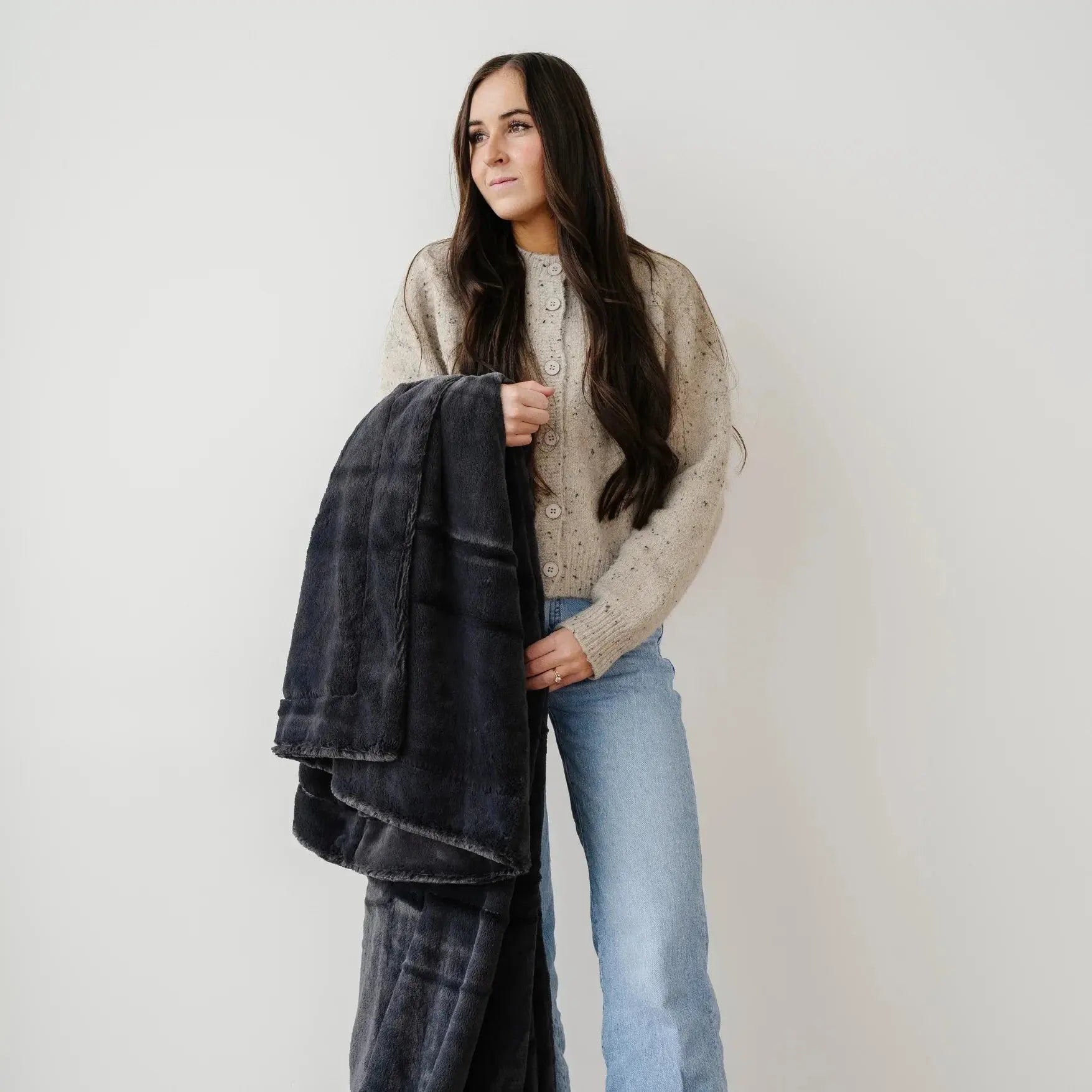 Woman holding a dark gray jacket against a plain background