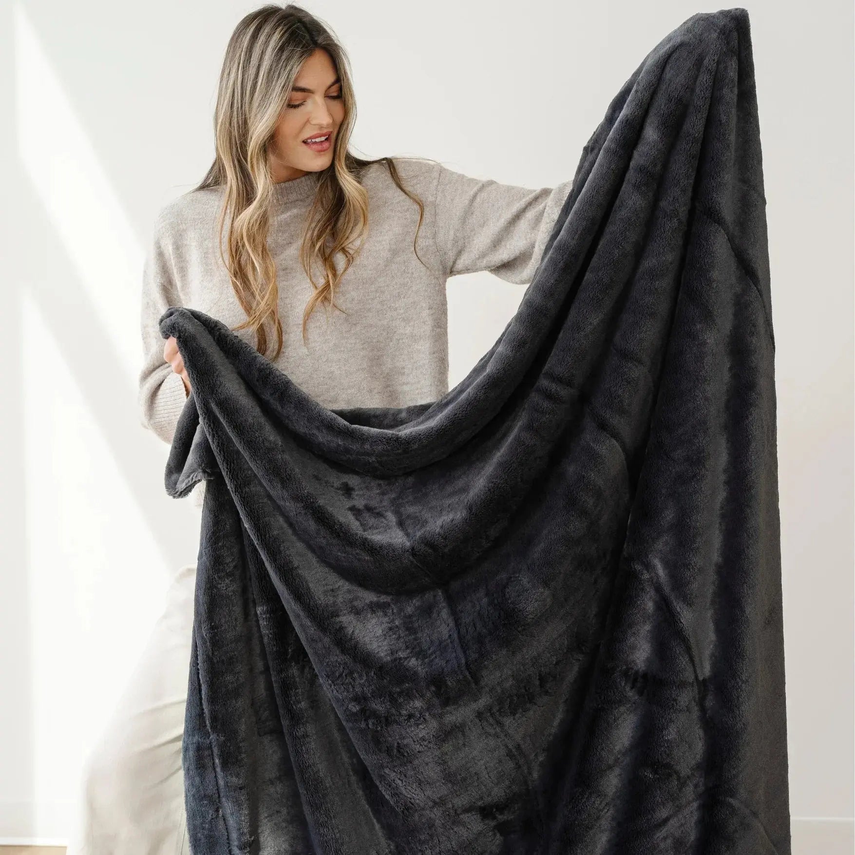Woman holding a large dark gray blanket against a white background