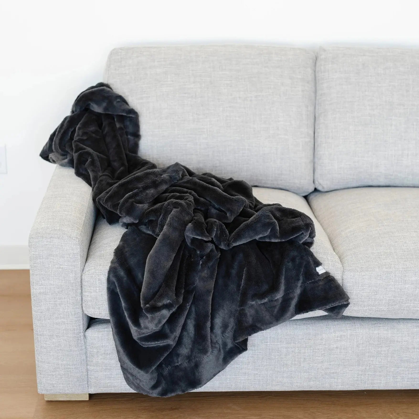 Dark gray plush blanket draped over a light gray sofa against a white wall.