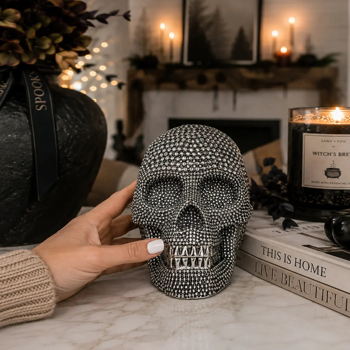 Decorative skull with rhinestones held by a hand in a Halloween-themed setting.