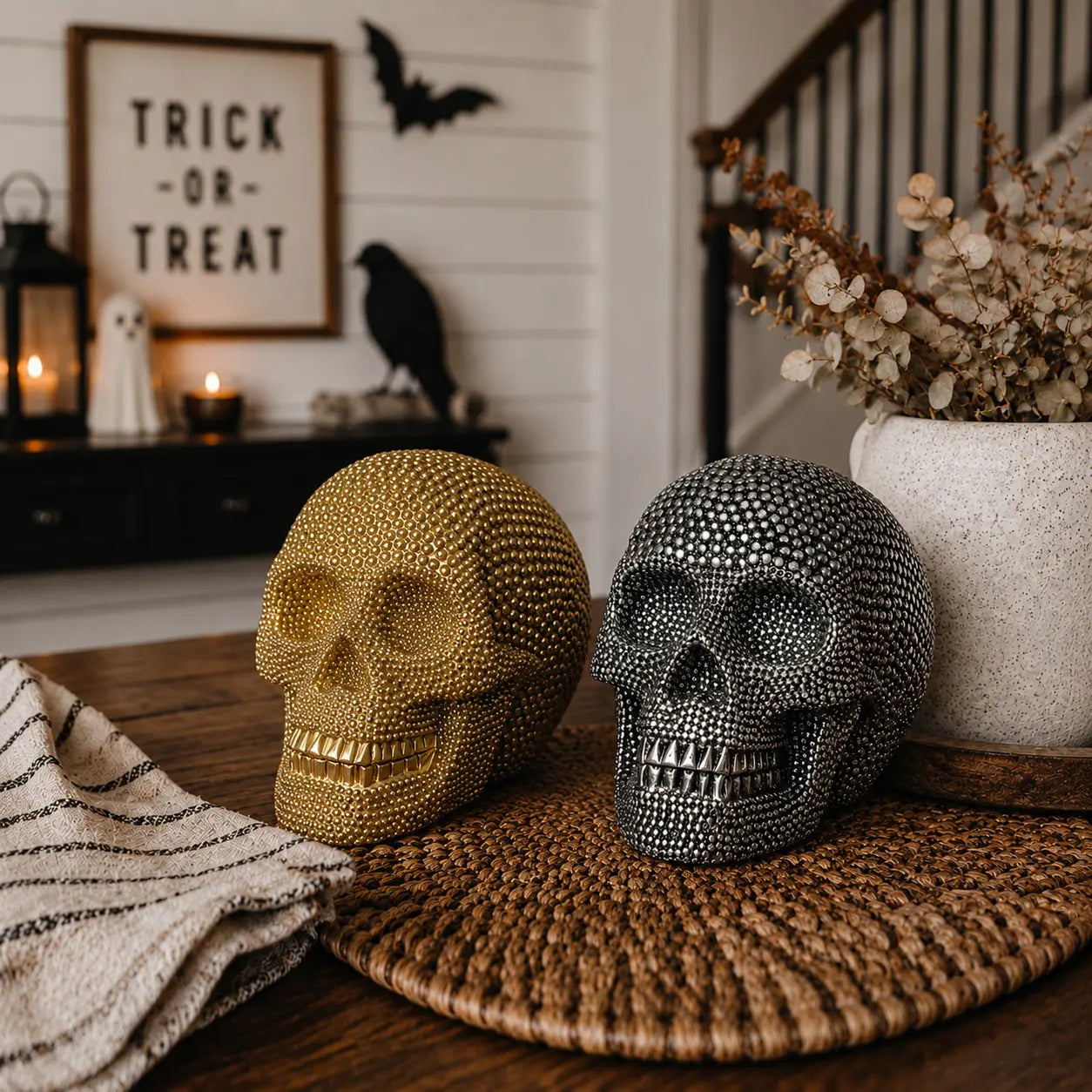 Decorative gold and silver skull sculptures on a table with Halloween decorations in the background.