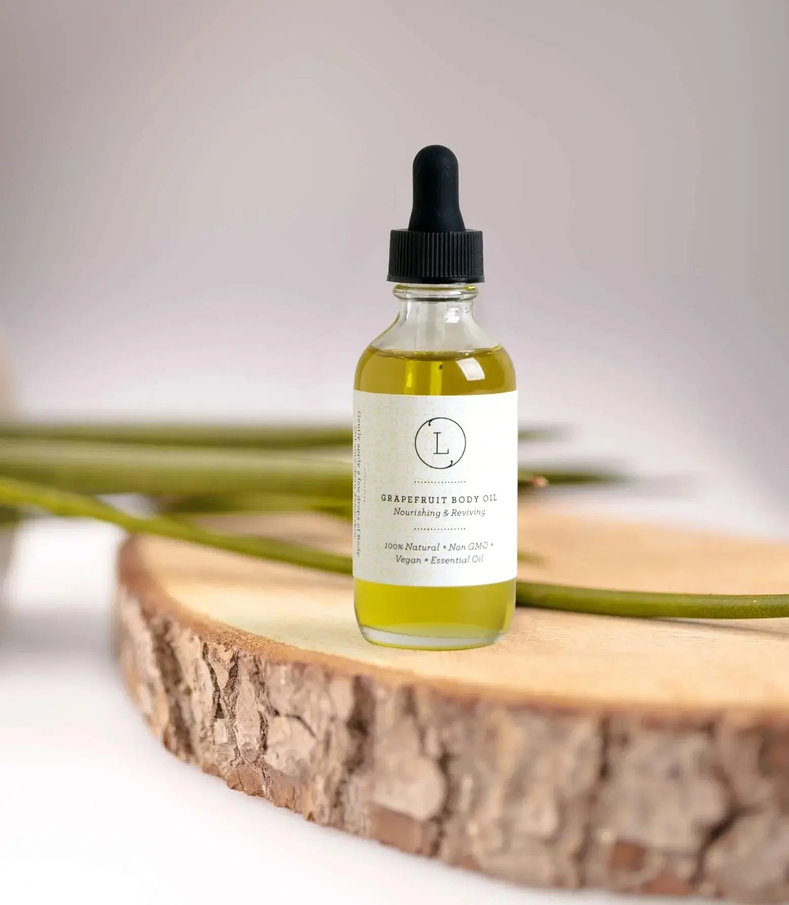 Grapefruit body oil in glass dropper bottle on wooden slice, natural vegan skincare for cozy home spa