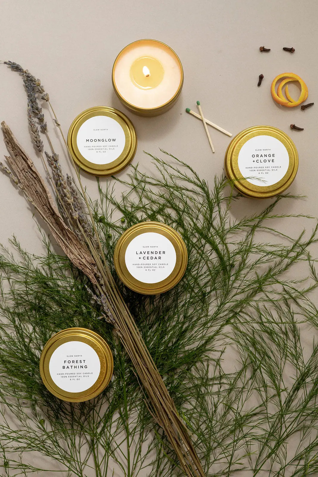 Cozy soy candles in gold tins with lavender, cedar, orange clove scents, styled with dried herbs for farmhouse home decor