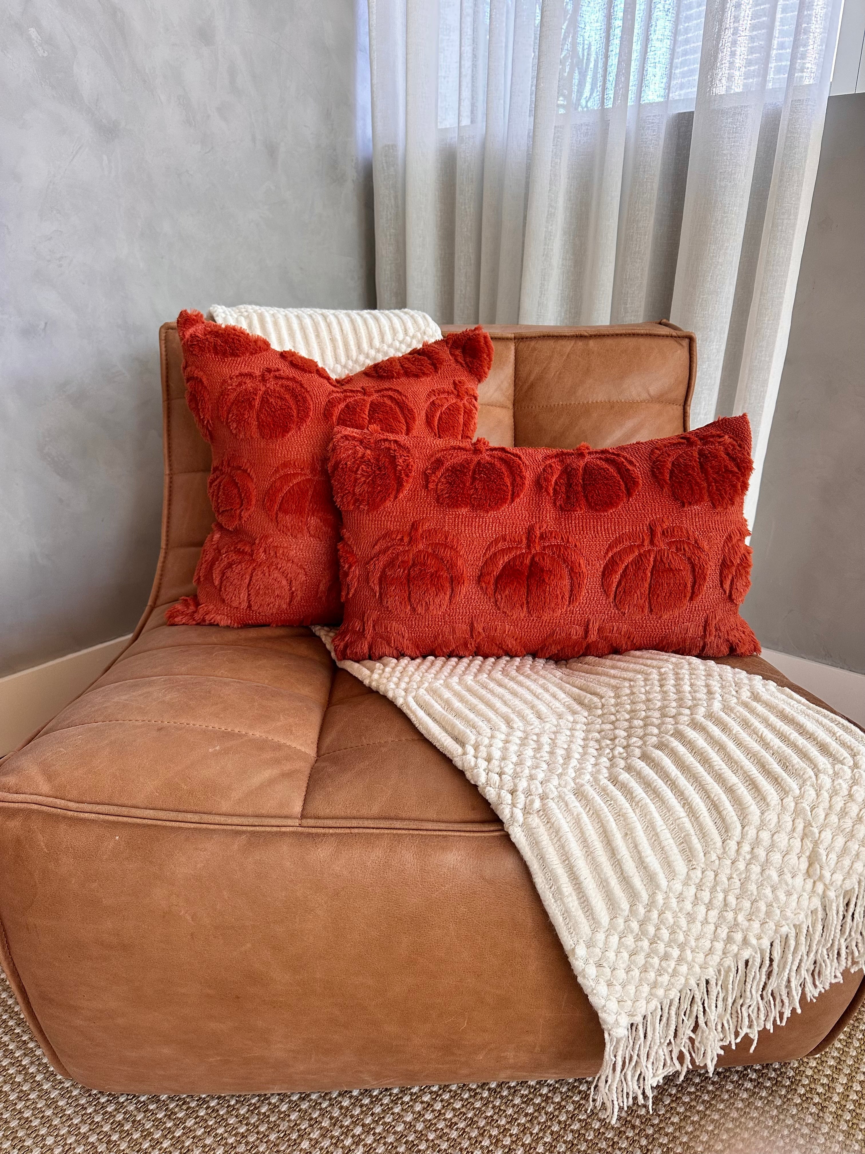 Brown leather chair with red textured pillows and a white blanket
