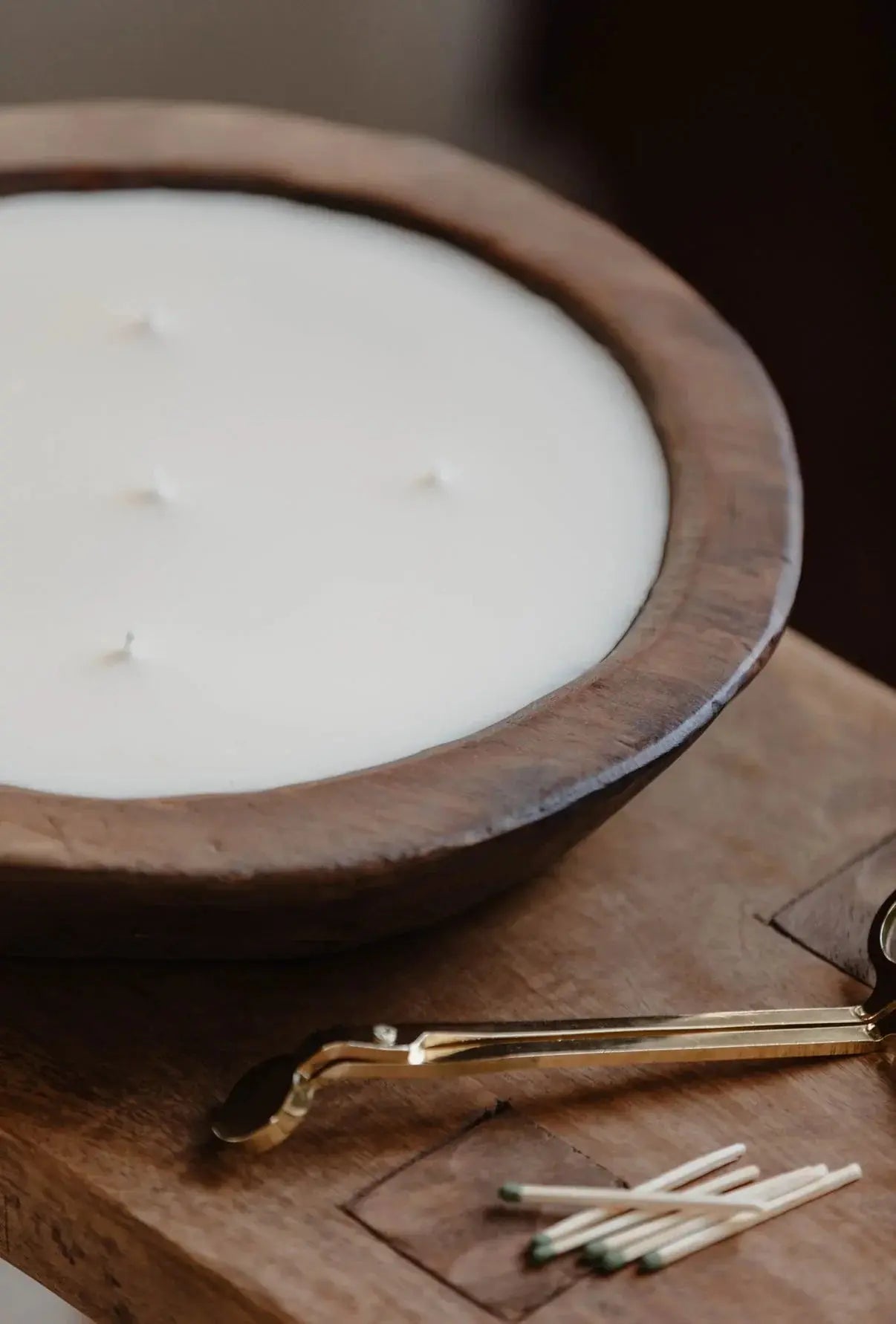 Large white candle in rustic wooden bowl with gold wick trimmer and matches, cozy farmhouse decor