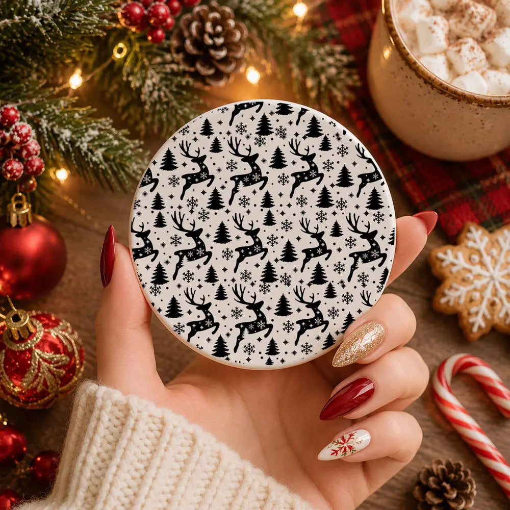 Hand holding a round coaster with reindeer pattern, surrounded by Christmas decorations and hot chocolate.